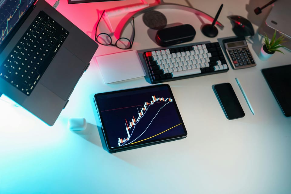 a desk of instruments such as a macbook or an ipad and iphone showing charts of the financial markets.